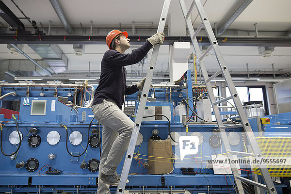 Junge Techniker klettern eine Leiter in einer Industriehalle hinauf