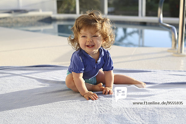 Porträt eines kleinen Mädchens auf einem Handtuch vor dem Schwimmbad