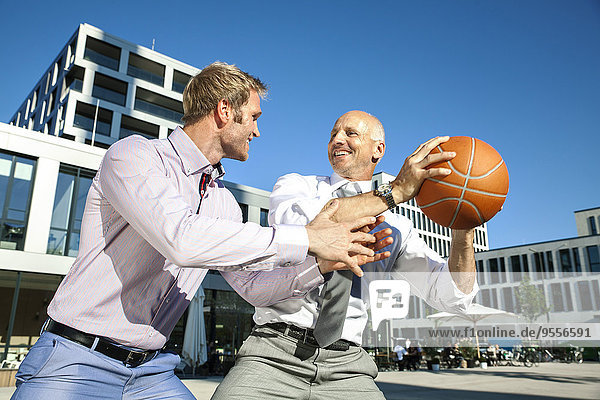 Two businessmen playing basketball outdoors