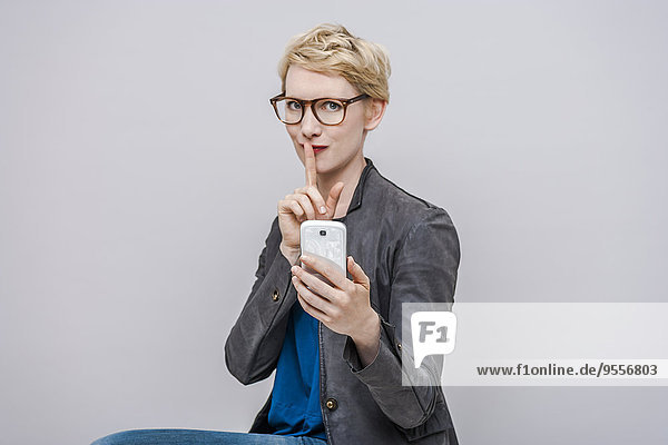 Porträt einer blonden Frau mit Finger auf dem Mund vor grauem Hintergrund