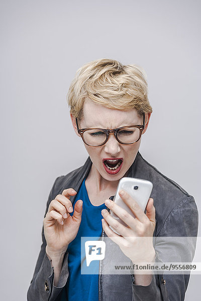Porträt einer blonden Frau  die ihr Smartphone schreiend ansieht.
