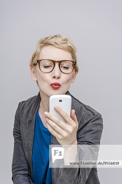 Blonde Frau mit schmollendem Mund  die einen Selfie mit ihrem Smartphone nimmt.