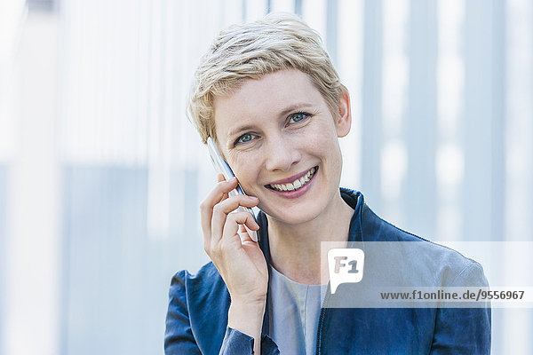 Porträt einer lächelnden blonden Frau beim Telefonieren mit dem Smartphone