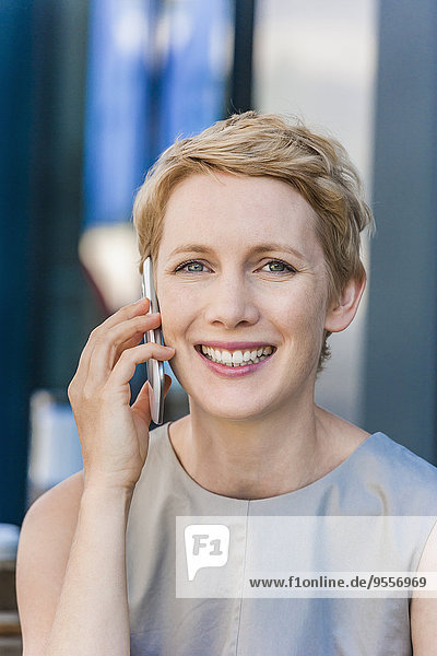 Portrait of smiling blond woman telephoning with smartphone
