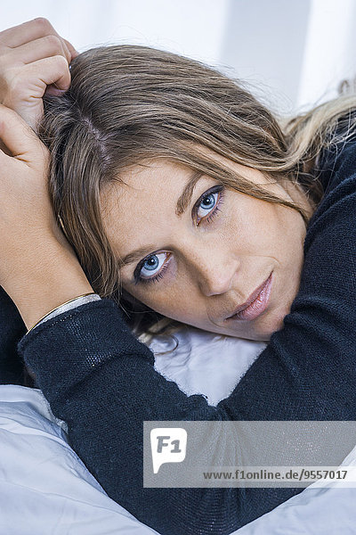 Porträt einer blonden Frau mit blauen Augen auf dem Bett liegend  Nahaufnahme