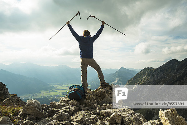 Österreich  Tirol  Tannheimer Tal  junger Mann mit Wanderstöcken jubelnd auf der Bergspitze