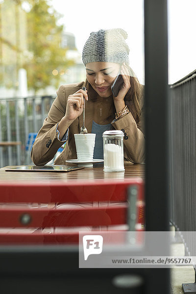 Junge Frau sitzt auf dem Bürgersteig Cafe Telefonieren mit Smartphone