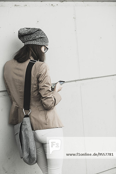Junge Frau lehnt sich an eine Wand und liest SMS.
