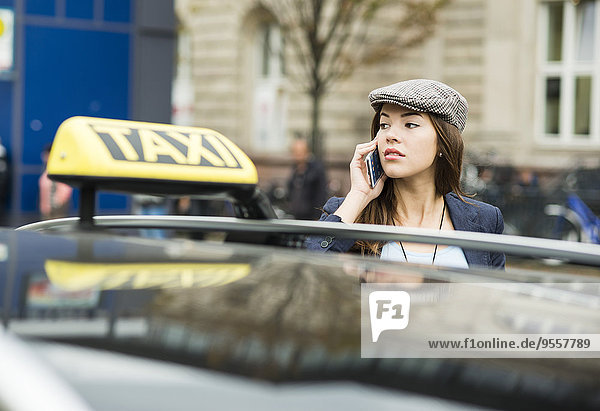 Junge Frau telefoniert mit Smartphone hinter dem Taxi