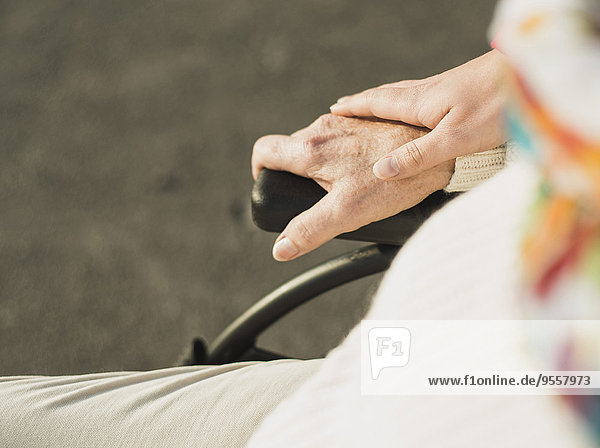 Hand der jungen Frau auf Hand der älteren Frau im Rollstuhl sitzend