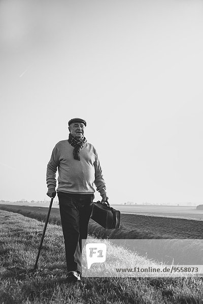 Älterer Mann mit Tasche beim Wandern in ländlicher Landschaft