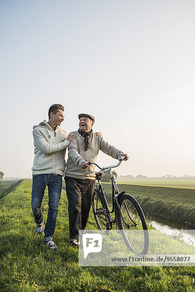 Senior Mann und Enkel in ländlicher Landschaft mit Fahrrad