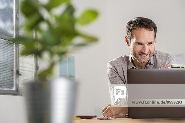 Lächelnder Geschäftsmann beim Blick auf Laptop im Büro