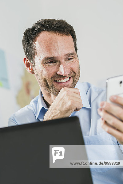 Smiling businessman with laptop and cell phone in office