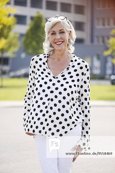 Porträt der lächelnden Seniorin in weißer Bluse mit schwarzen Punkten