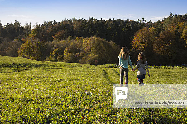 Germany  Bavaria  Landshut  two girls walking on meadow in autumn
