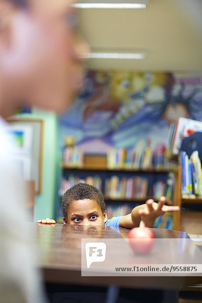 Junge in der Bibliothek schaut auf den Apfel