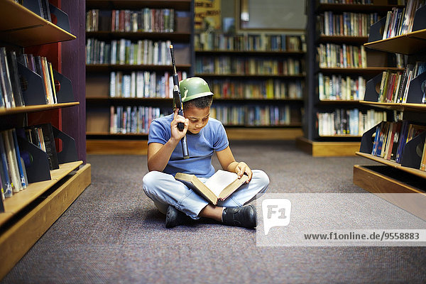 Boy with helmet and gun reading book in library
