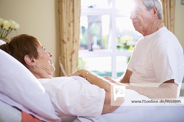 Seniorenfrau im Krankenhausbett im Gespräch mit Seniorenmann