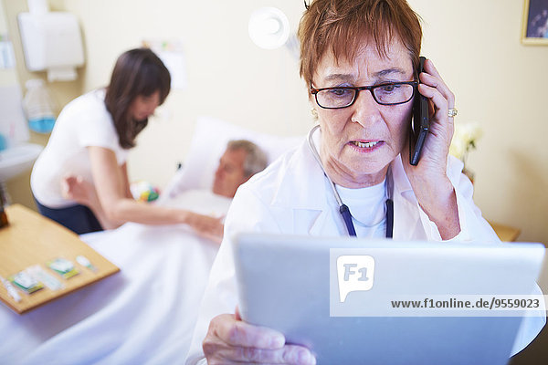 Arzt mit Handy und digitalem Tablett im Krankenhauszimmer