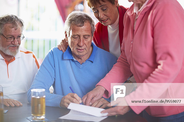 Älterer Mann mit Freunden beim Unterschreiben des Dokuments