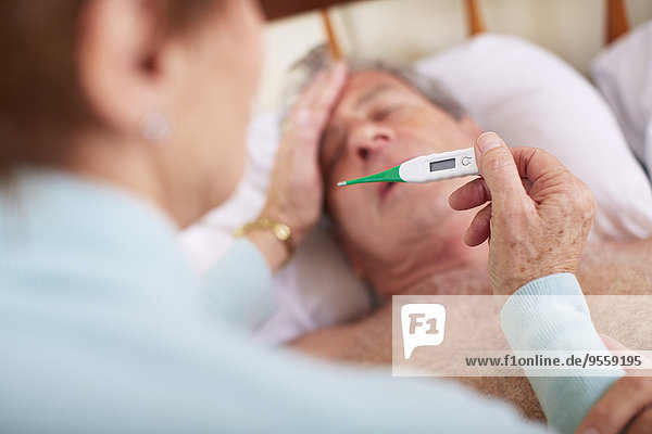 Senior woman taking temperature of sick husband at home