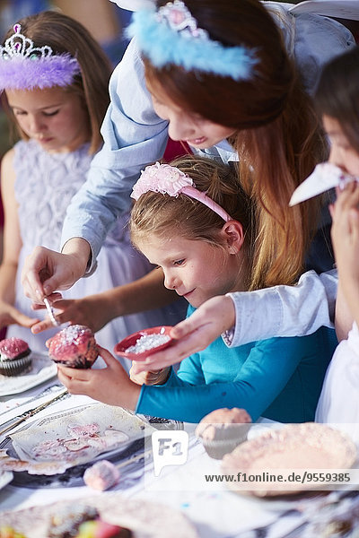 Teenagermädchen und Mädchen beim Garnieren von Muffins auf einer Geburtstagsparty