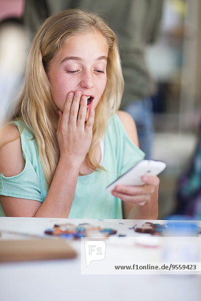 Überraschtes Mädchen in der Kunstklasse beim Betrachten des Handys