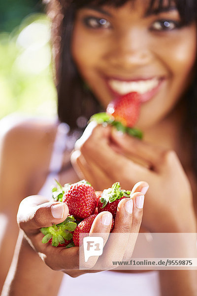Hand einer lächelnden Frau die Erdbeeren hält.