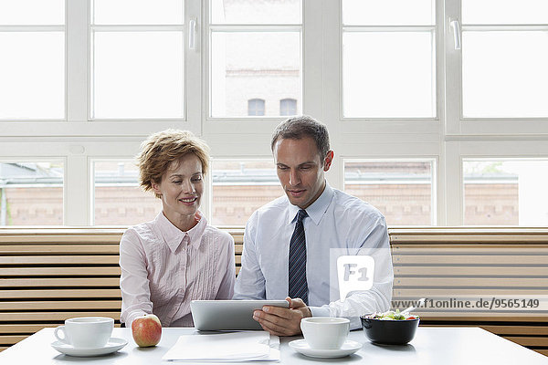 Geschäftskollegen  die ein digitales Tablett während eines Geschäftsessens verwenden