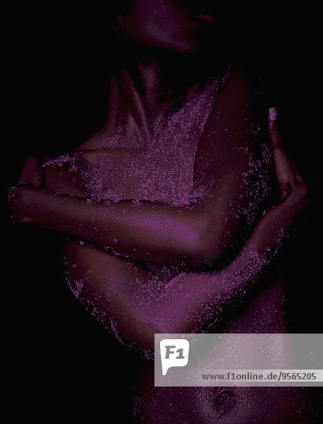 Mittelteil der nackten Frau mit rosa Puder auf dem Körper vor schwarzem Hintergrund