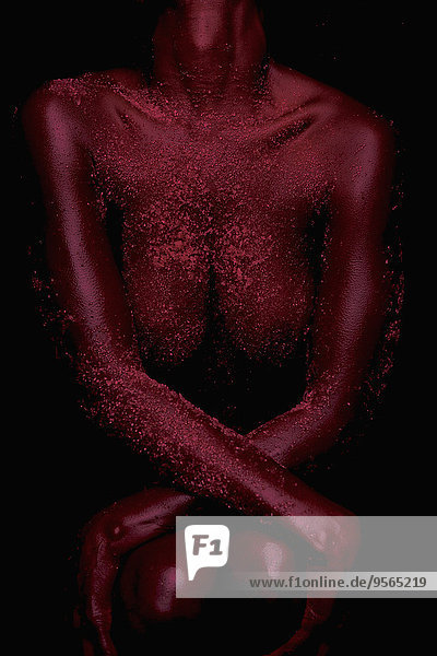 Mittelteil der nackten Frau mit rosa Puder auf dem Körper vor schwarzem Hintergrund