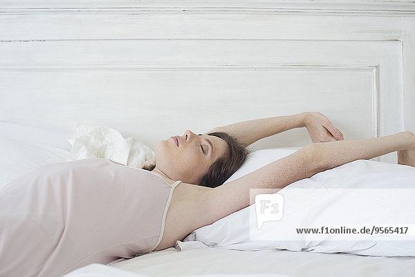 Woman lying on back in bed stretching