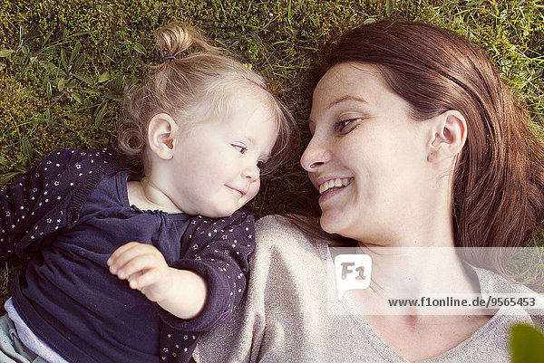 Mutter und kleines Mädchen liegen auf Gras und lächeln sich an.