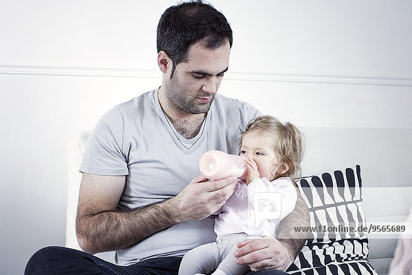 Father holding baby girl on lap  feeding her with bottle