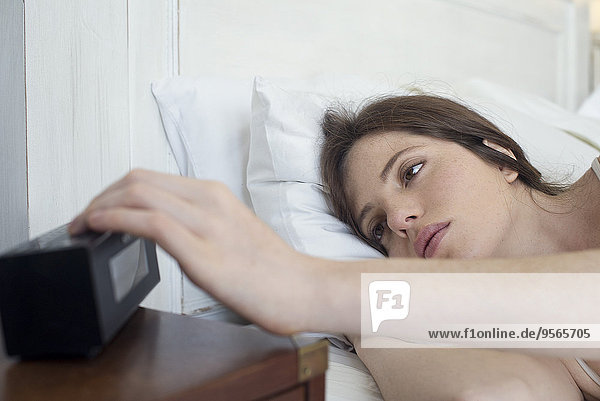 Frau im Bett drückt Wecker Schlummertaste