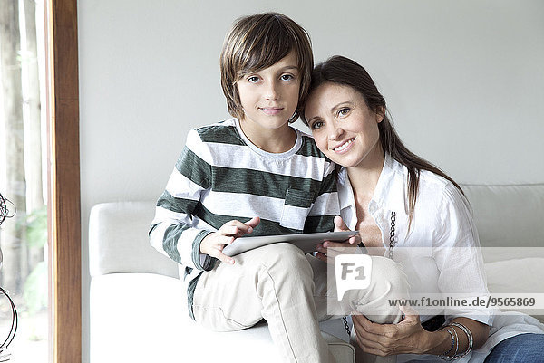 Mutter und Sohn sitzen zusammen auf dem Sofa mit digitalem Tablett