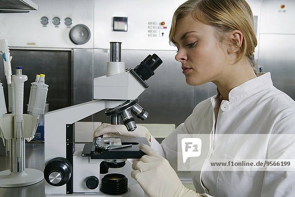 Eine Frau  die durch ein Mikroskop schaut.