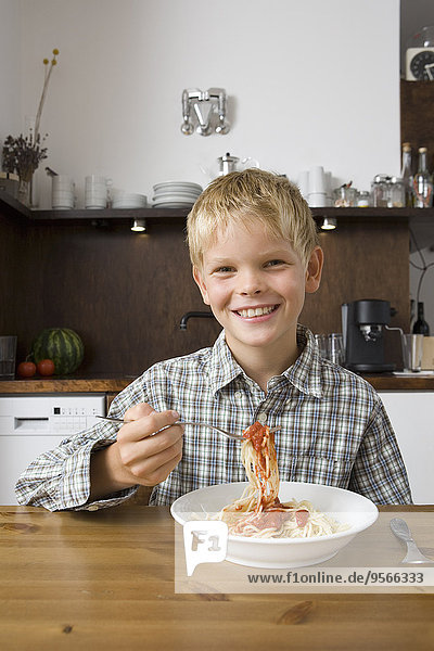 Junge sitzt am Tisch und isst Spaghetti Bolognese