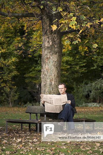Ein reifer Mann sitzt auf einer Parkbank und liest eine Zeitung.