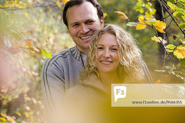 Mittleres erwachsenes Paar  das sich zwischen Zweigen mit Herbstblättern umarmt.