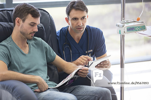 Arzt mit digitalem Tablett  im Gespräch mit einem Patienten  der sich im Krankenhaus in Behandlung befindet.