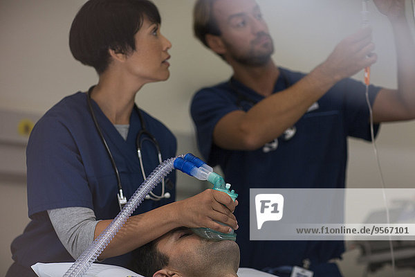Doctor holding oxygen mask over patient  doctor adjusting IV drip in intensive care unit