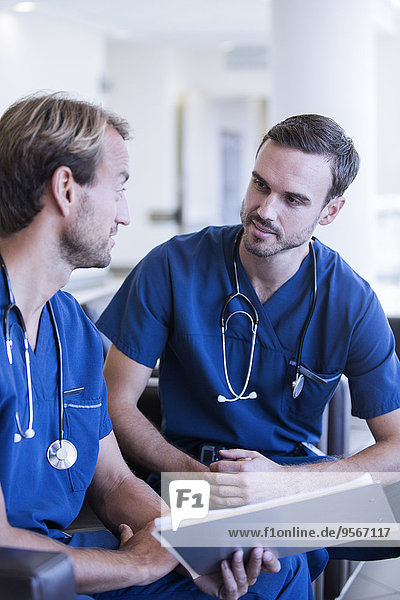 Two male doctors with stethoscopes  wearing scrubs talking in hospital