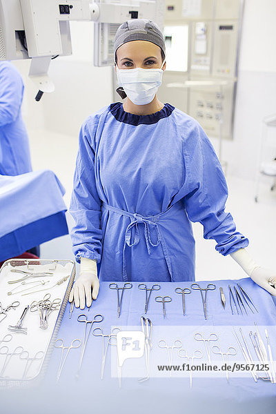Portrait of surgical nurse standing behind medical tools on table in operating theater