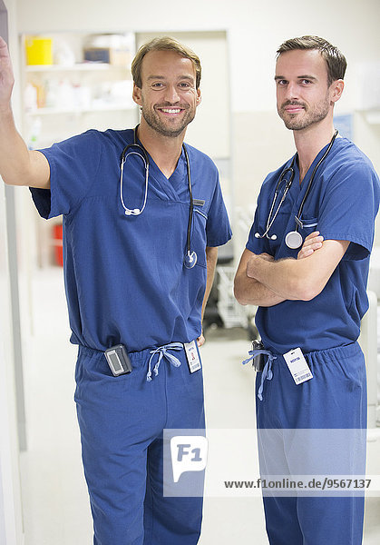 Two smiling male doctors wearing scrubs standing in hospital ward