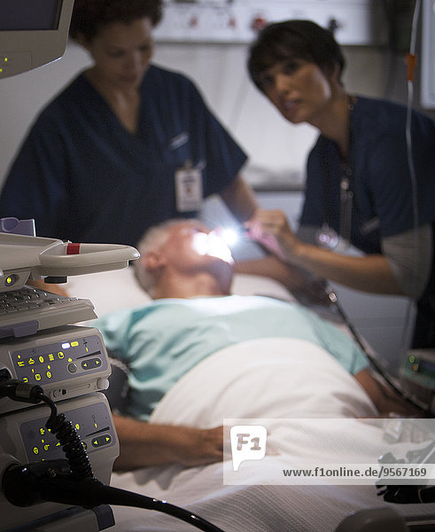 Arzt untersucht älteren Patienten mit Taschenlampe auf der Intensivstation