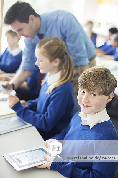 Porträt eines Schülers mit digitalem Tablett im Klassenzimmer  Kinder und Lehrer im Hintergrund