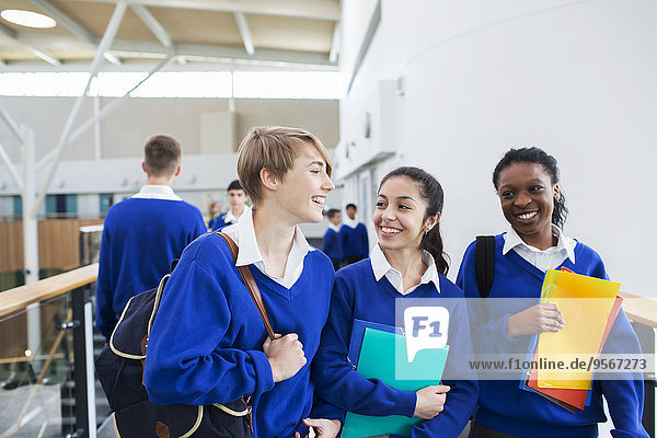 Smiling female students wearing school uniforms walking through school corridor