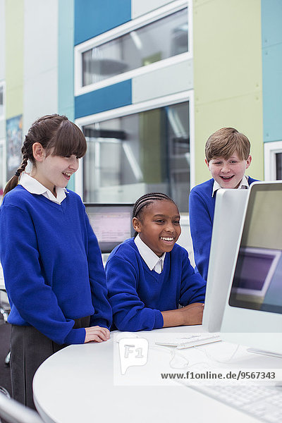 Grundschulkinder schauen auf den Computer und lächeln